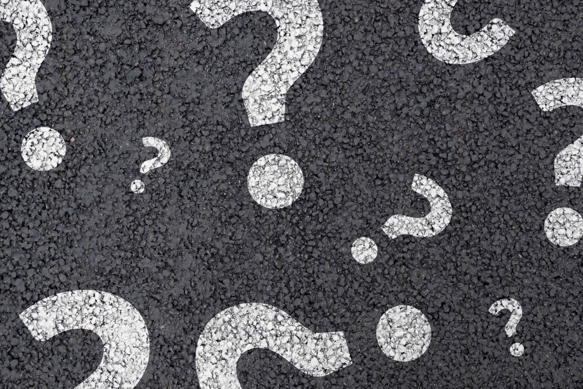 Closeup on an asphalt service painted with white question marks.