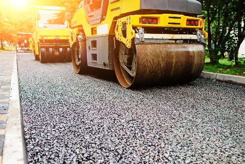 Asphalt paving heavy equipment drives over a stretch of asphalt road being paved. 