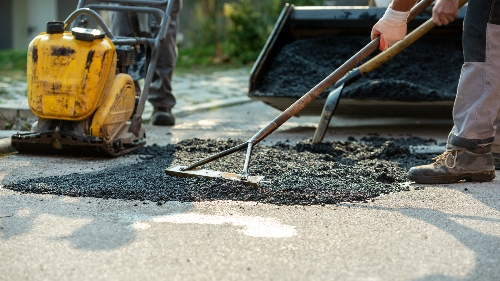 A worker uses a pressing machine to finish an asphalt paving project.