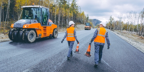 A professional asphalt paving contractor crew lays out road blocks while paving a stretch of highway.