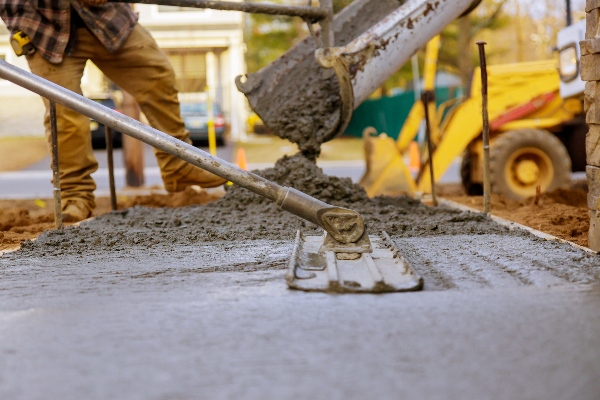 Some construction workers standby while pouring and smoothing concrete into a paving project zone.