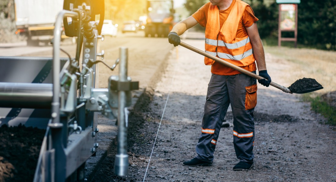 A construction worker shoveling fresh asphalt onto a road.