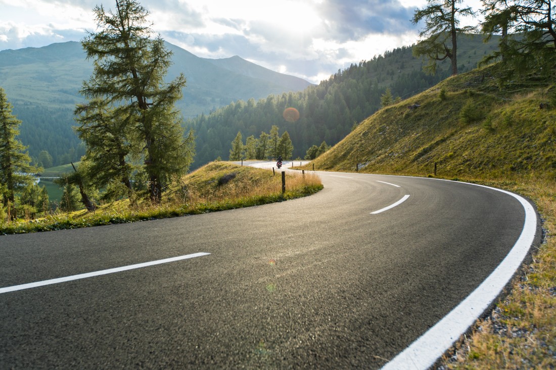 An asphalt road on a hot summer day with trees and mountains. 