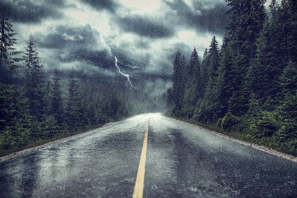 A dark and stormy night pours rain onto an asphalt-paved surface. 